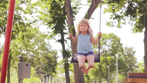 una niña columpiándose en el parque, cámara lenta, caluroso día de verano, ángulo bajo