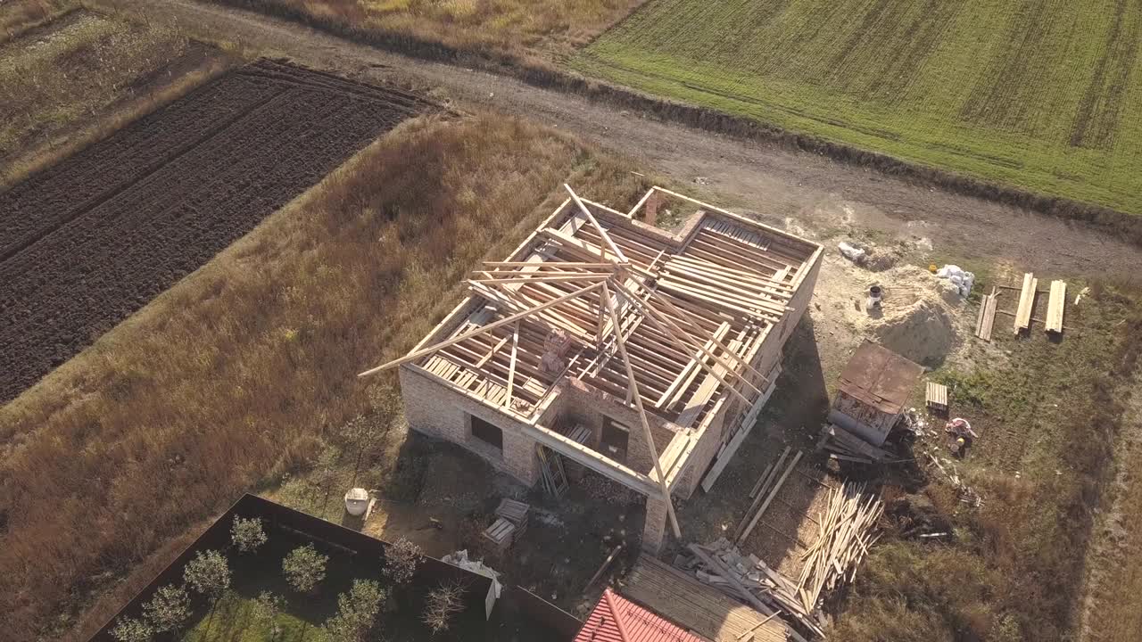 Oversiktsbilde av to private hus, ett under konstruksjon med treramme for taktekking og et annet ferdig med rødt teglsteinstak.