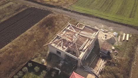 top down aerial view of two private houses, one under construction with wooden roofing frame and another finished with red tiled roof.