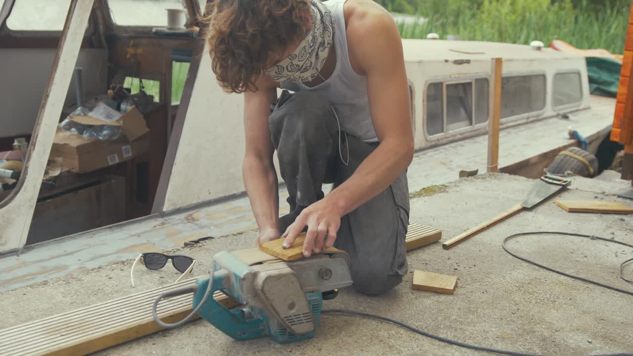 Sanding wooden block using belt sander boat maintenance outdoors, MID SHOT