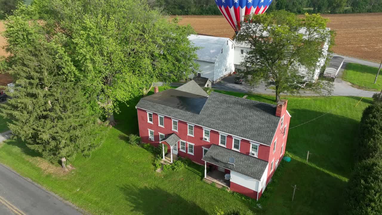 disparo de avión no tripulado ascendente de una casa en el campo estadounidense y aterrizaje de globo de aire caliente en un campo agrícola en el fondo - disparo aéreo ascendente