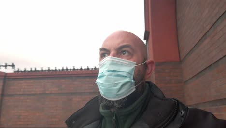 Male-security-guard-wearing-protective-corona-virus-medical-PPE-mask-right-pan-against-brick-wall