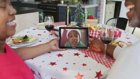 Lächelndes-Afroamerikanisches-Paar,-Das-Ein-Tablet-Für-Einen-Weihnachtsvideoanruf-Mit-Einem-Jungen-Auf-Dem-Bildschirm-Verwendet