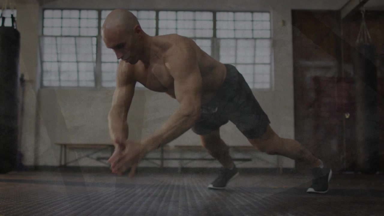 Male trainer performing alternating reach push-ups on rubber floor, starting lowered for fitness