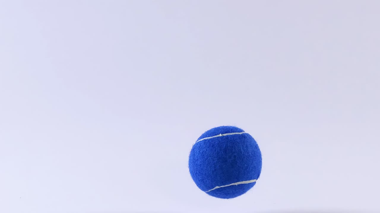 A blue ball captured mid-air against a plain white background, showcasing its motion and trajectory.