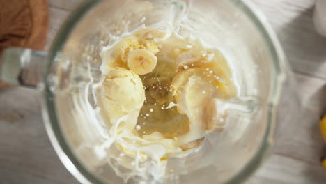 vanilla ice cream and banana milkshake mixed in a glass blender in slow motion, top view, inside of the device