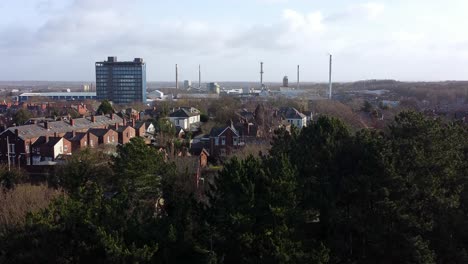 Vista-Aérea-Que-Se-Establece-Sobre-Los-árboles-Del-Parque-Hasta-El-Paisaje-Urbano-Industrial-Con-El-Rascacielos-Blue-Pilkingtons,-Merseyside,-Inglaterra