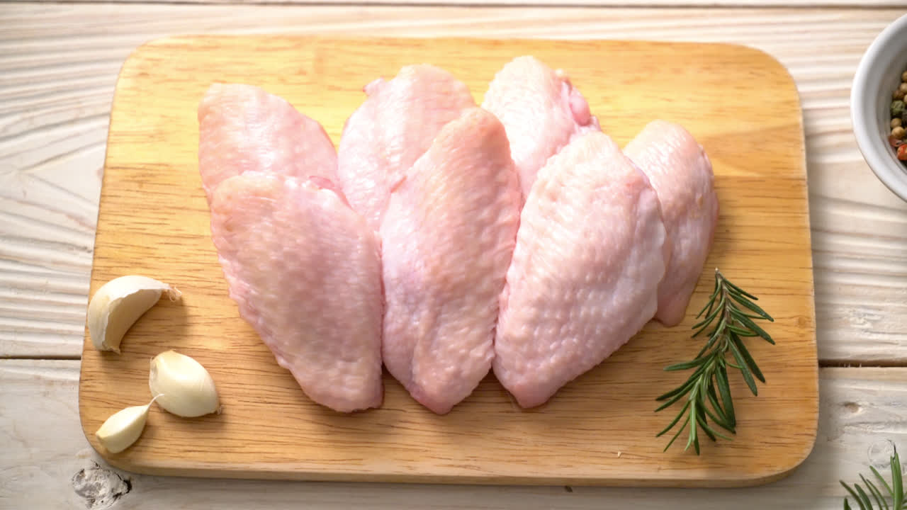 Alas de pollo medio crudo fresco sobre tabla de madera con ingredientes