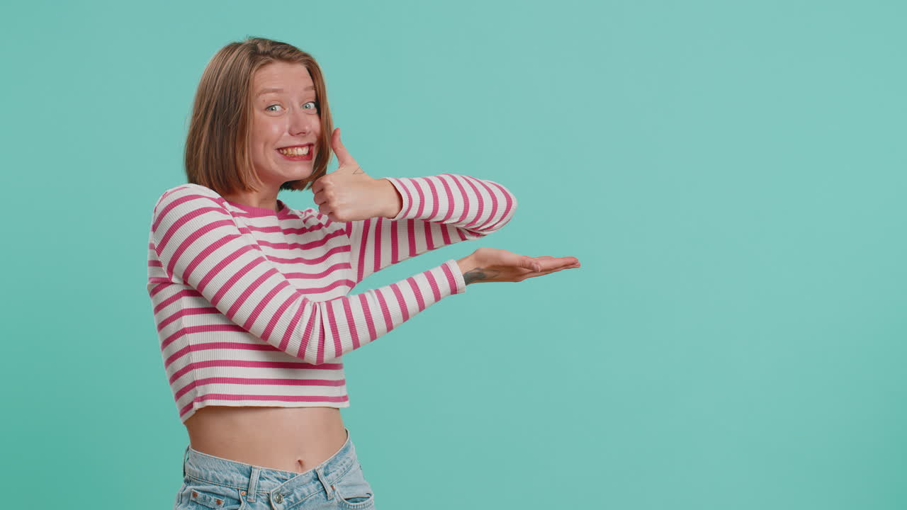 mujer joven mostrando los pulgares hacia arriba y señalando a la izquierda en el espacio en blanco lugar para su logotipo de publicidad