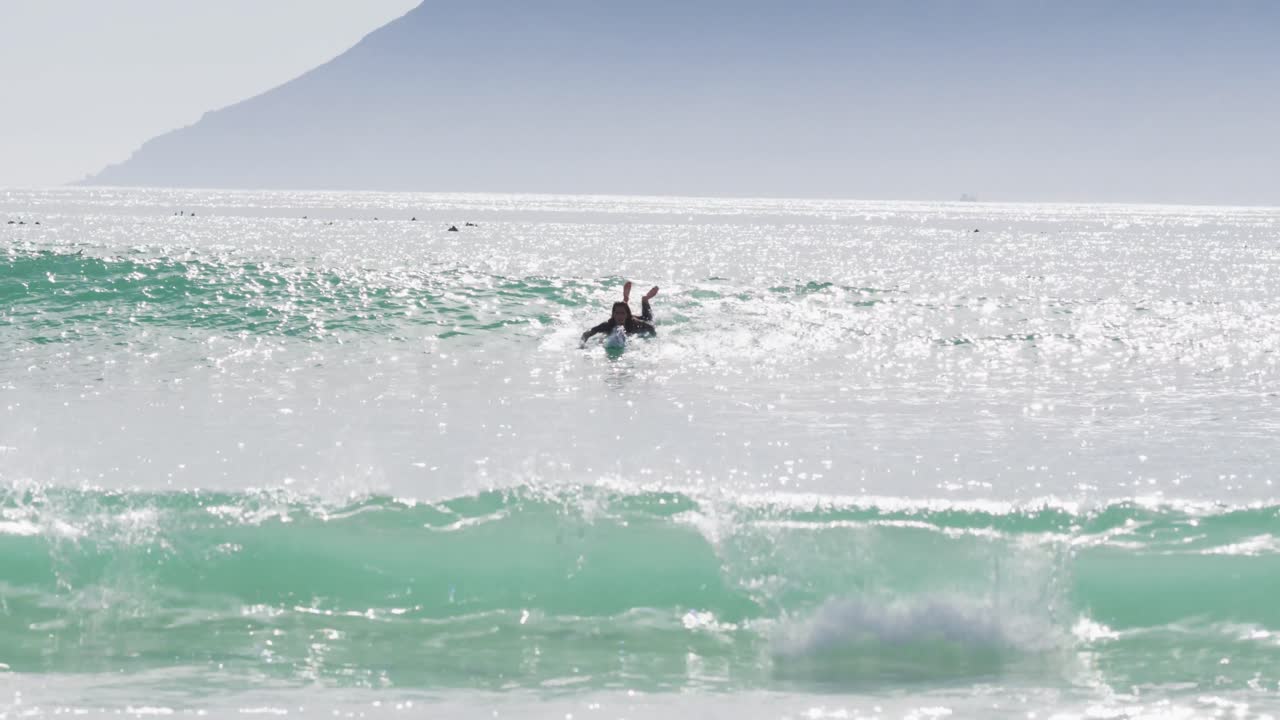 Mixed race woman lying on surfboard paddling in the sea