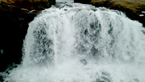 A-close-up-view-of-a-waterfall-in-Iceland's-mountains,-resembling-a-flowing-curtain,-is-captured-as-the-camera-zooms-in-rapidly