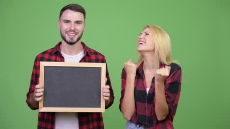 young couple holding blackboard and looking excited together