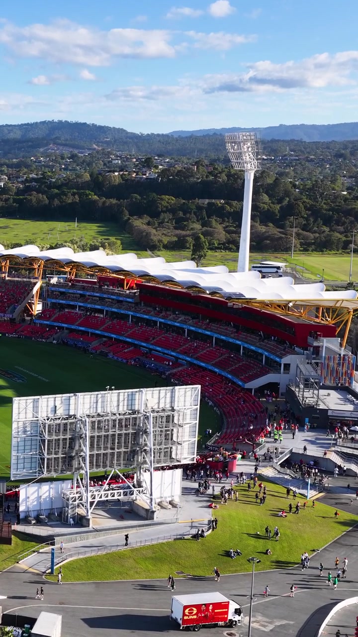 High-angle wide shot of a contemporary sports arena under bright daylight with surrounding hills.