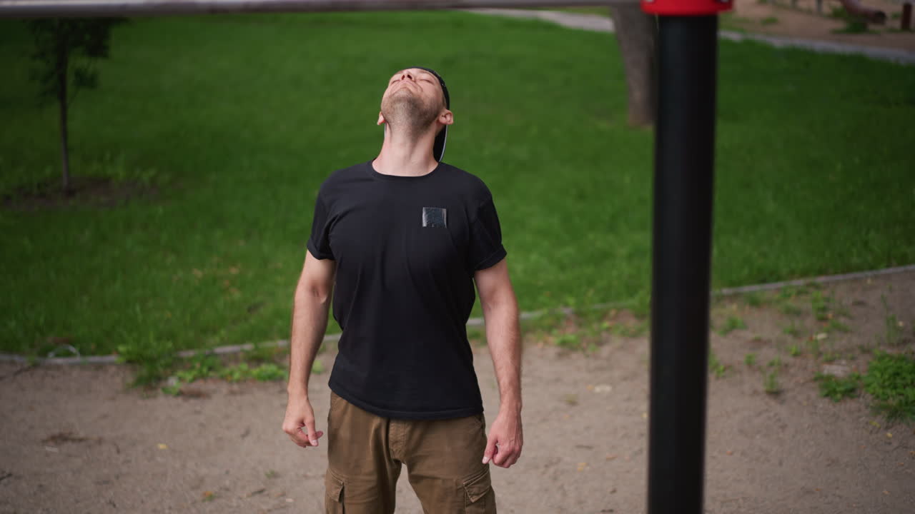 Man Stretches Neck At Urban Fitness Park, Park Athlete Prepares With Warmup Near Pullup Station, Caucasian Man Engages In Controlled Warmup Exercises Beside Outdoor Fitness Equipment