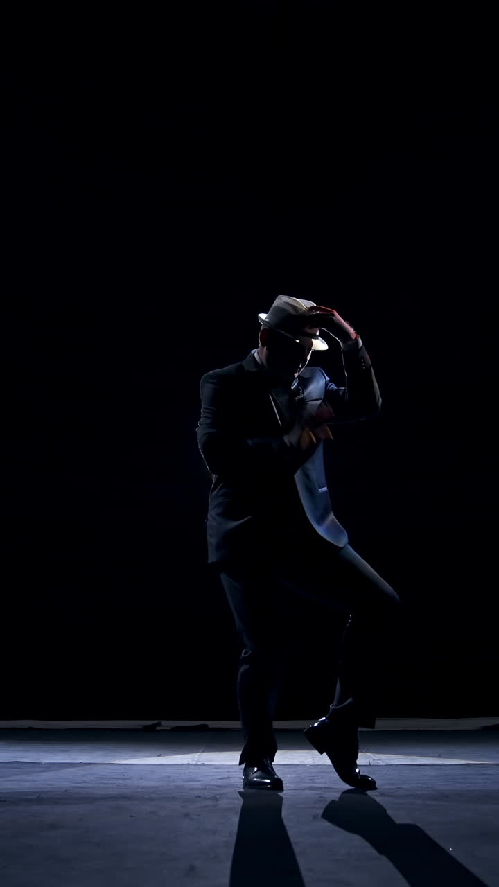 Actor making funny dance on a stage. Silhouette of a man in costume and hat dancing in dark background. Amusing performance on scene. Vertical video