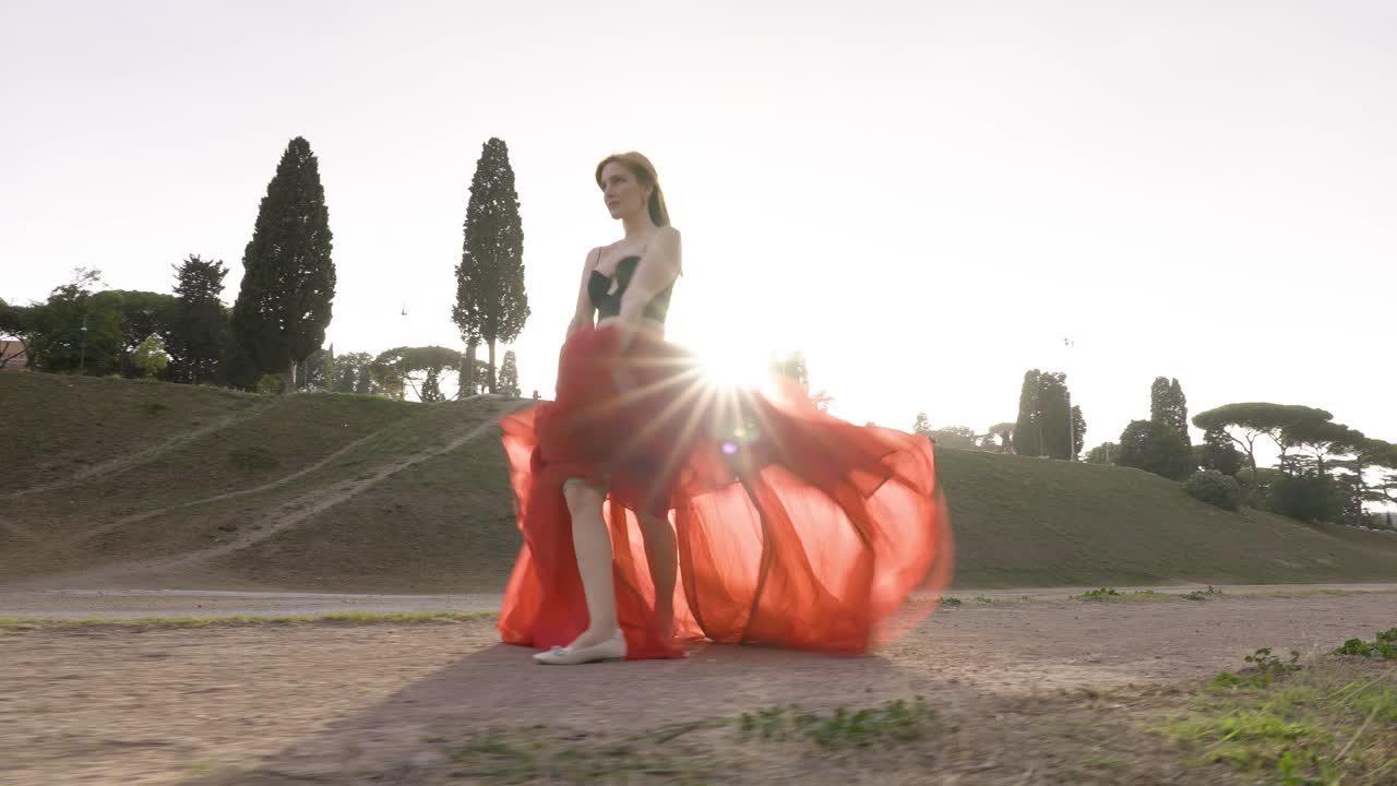 Woman dancing in the beautiful sunshine - girl wearing a red dress and black top on a gravel road