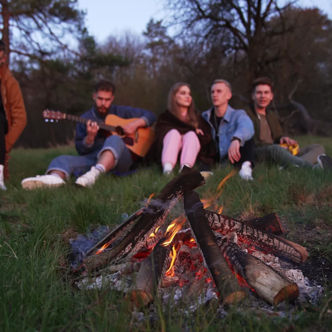Outdoor campfire having fun friends. Young lifestyle people sitting near the bonfire