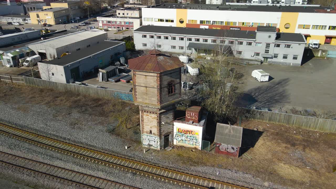 Aerial drone footage orbiting and spinning around an old gray abandoned brick railroad or train conductor watchtower or tower during a sunny spring or autumn day in Estonia Tallinn väike urban area.