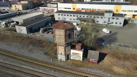 aerial drone footage orbiting and spinning around an old gray abandoned brick railroad or train conductor watchtower or tower during a sunny spring or autumn day in estonia tallinn väike urban area.