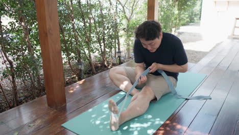 asian man pulling yoga strap to stretch his leg and back