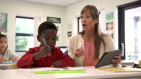 teacher using tablet helping student with schoolwork in classroom, focused learning