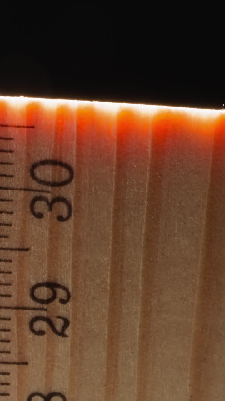Bright orange light at end of wooden ruler on black background. Straight strip made of wood material used for measuring distances and things macro