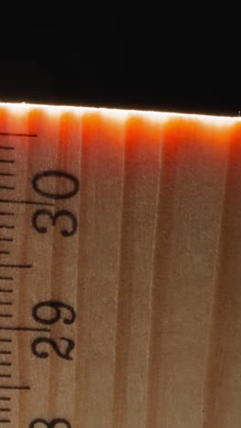 bright orange light at end of wooden ruler on black background. straight strip made of wood material used for measuring distances and things macro