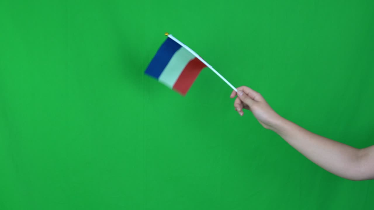 Primo piano di una mano sconosciuta che tiene una bandiera francese sventolante su sfondo green screen in studio. Ripreso in risoluzione 4k.