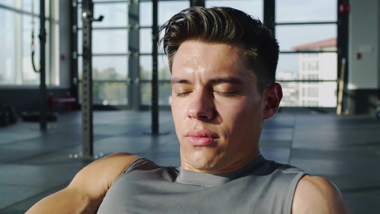 Starting low, trainee doing crunches in gym, wearing sleeveless gray top, training near squat rack