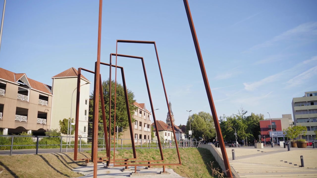 Perspective view of a geometric metal art installation surrounded by urban architecture in Saarlouis Germany