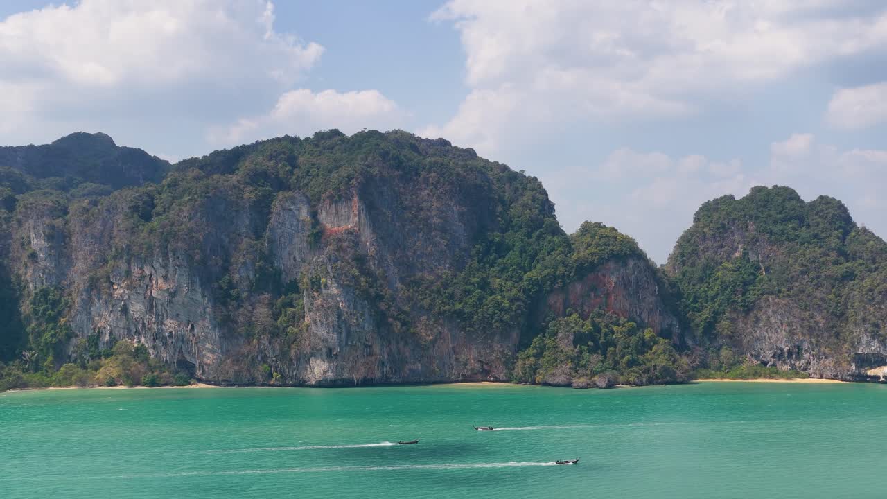 Ampia ripresa aerea di scogliere calcaree e acqua turchese con barche che passano a Krabi, Thailandia