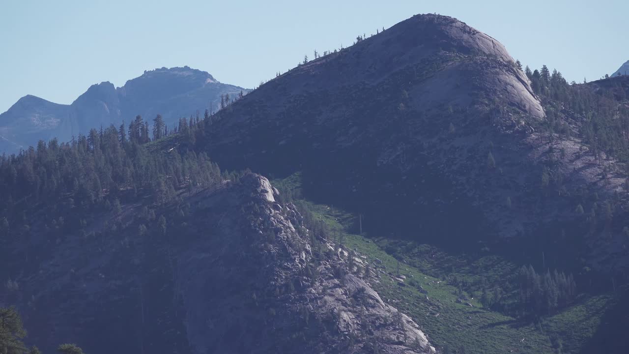 Gradual zoom out highlighting rocky peaks, sloping granite domes, and patches of forest within the high sierra range