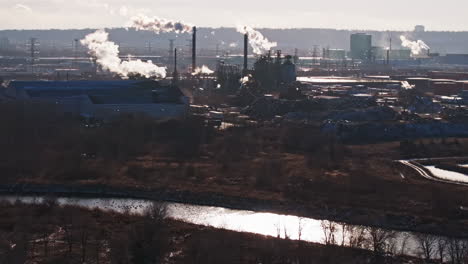 Complejo-Industrial-A-Orillas-Del-Río-Con-Chimeneas-Que-Emiten-Vapor,-Retroiluminado-Por-La-Luz-Del-Sol,-Concepto-De-Impacto-Ambiental