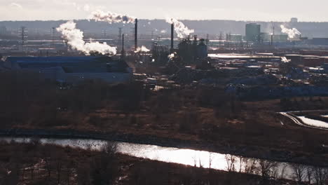 complejo industrial en la orilla del río con chimeneas que emiten vapor, iluminadas por la luz solar, concepto de impacto ambiental