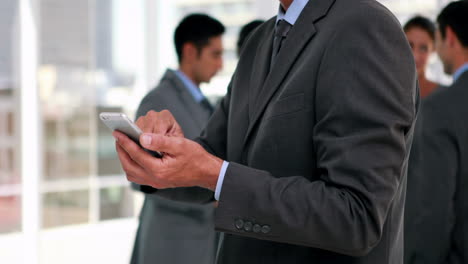 businessman using smartphone with his colleagues behind him