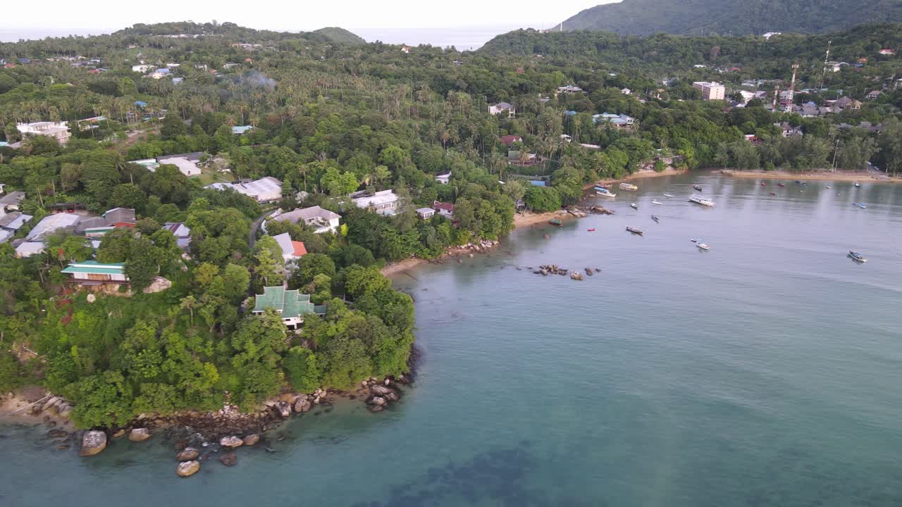 la antena de drones se mueve hacia atrás sobre el agua azul tropical con casas verdes en las laderas de las montañas en tailandia