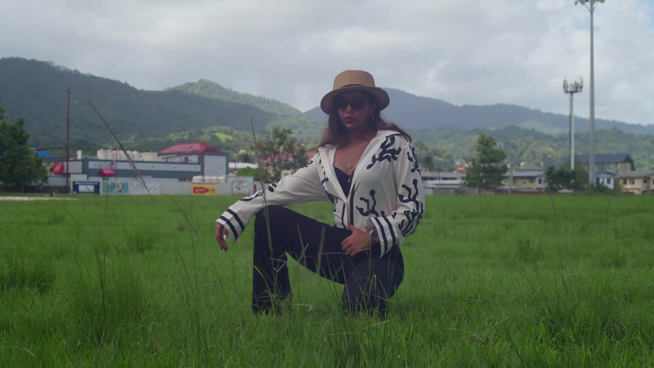 Vestita per il lavoro con pantaloni beige e una camicia bianca, una ragazza indossa un cappello da sole e legge in un parco in montagna durante la sua pausa pranzo.
