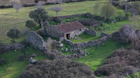 vuelo de avión no tripulado en el que visualizamos una vieja casa de piedra, probablemente para uso agrícola, rodeada de campos de cultivo abandonados, con casi todo el techo conservado y tiene un patio con una pared en madrid