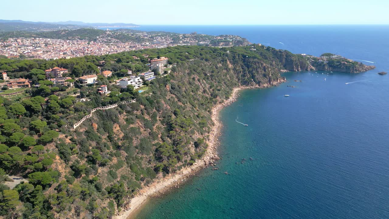 Aerial footage showing the beautiful coastline of san feliu de guixols in catalonia, spain, featuring turquoise mediterranean waters, verdant cliffs, and the coastal town in the background