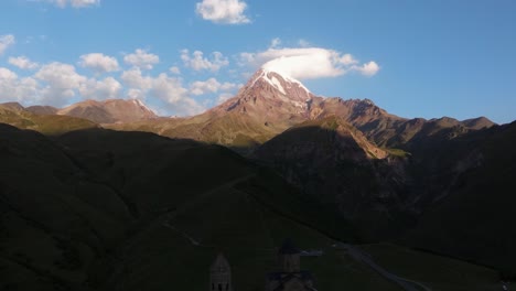 el retroceso aéreo revela la hermosa iglesia de la trinidad de gergeti, monte kazbek