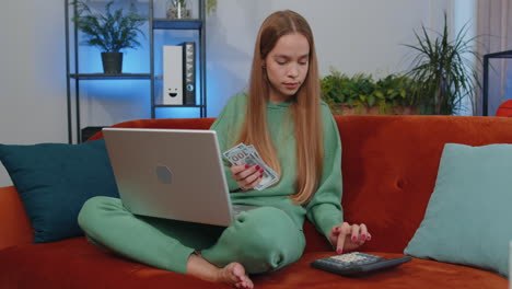 Smiling-happy-girl-counting-money-cash-and-use-laptop-pc-calculate-domestic-income-earnings-at-home