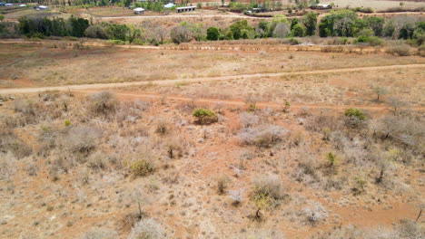 flying over a dry landscape with arid bushes towards solitary buildings in rural kenya