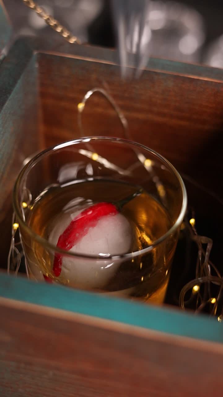 A whiskey cocktail in a wooden box with ice sphere