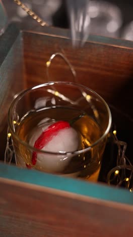 a whiskey cocktail in a wooden box with ice sphere