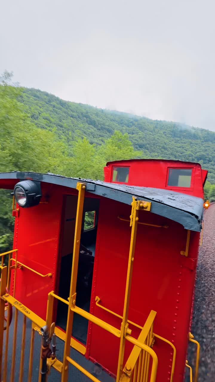 Gerbong Kereta Api Antik Merah Melaju Melintasi Hutan Pegunungan. Pemandangan Atas Atap dan Platform Gerbong Kereta Api Belakang Berwarna Merah Bergerak di Sepanjang Rel Kereta Api Melengkung di Lembah