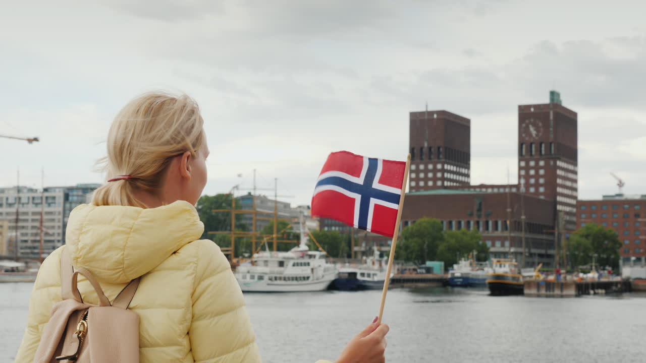 노르웨이 국기를 든 여성 관광객이 오슬로 시를 바라보며 부두에 서 있다