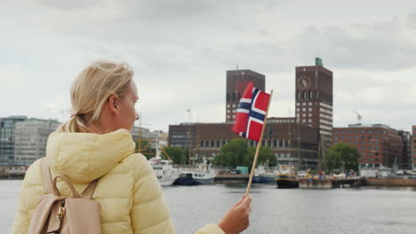 A-Female-Tourist-With-A-Flag-Of-Norway-Is-Standing-On-The-Pier-Looking-Forward-To-The-City-Of-Oslo-T