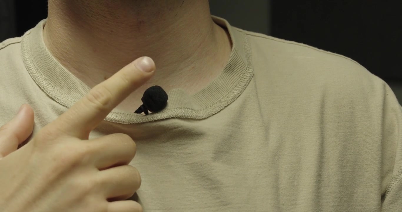 Primo piano di una persona che aggancia un microfono lavalier a una maglietta prima di registrare. Concetto di produzione audio, creazione di contenuti, trasmissione e attrezzature di registrazione