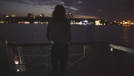 silhouette of a young attractive woman against a background of a night city aboard a boat