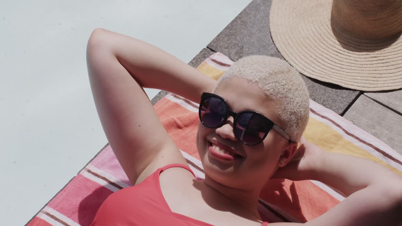 mujer biracial feliz con gafas de sol tomando el sol en una toalla en cámara lenta